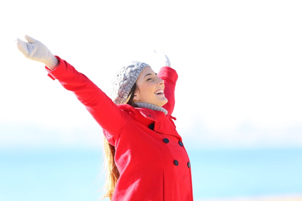 Woman in red coat on beach celebrating good health and understanding cholesterol.